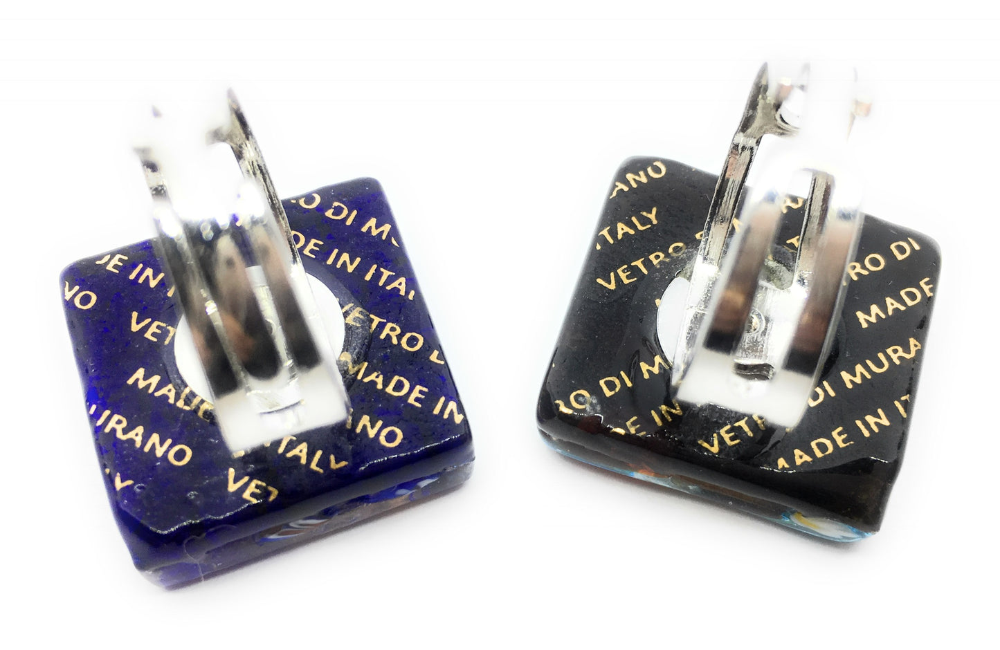Two square rings crafted from Murano Glass by Murano Passion, featuring metallic bands with one in dark blue and the other in black, proudly display gold inscriptions "MADE IN ITALY" and "VETRO DI MURANO." These Millefiori Rings on Silver Leaf are genuine pieces from Venice, elegantly set upright against a white background to emphasize their handmade allure.