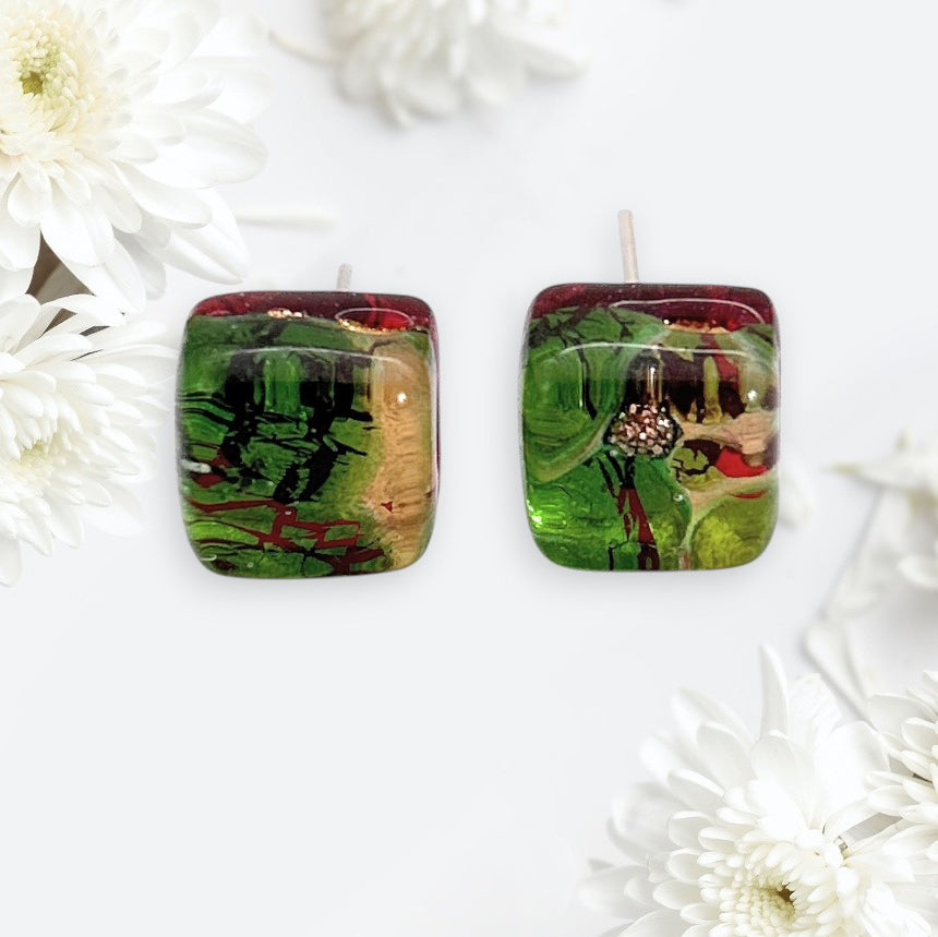 A pair of Murano Passion Murano Glass Earrings - Green/Gold, Dainty 8mm (MGE19), featuring abstract patterns, is displayed on a white background surrounded by white chrysanthemum flowers.