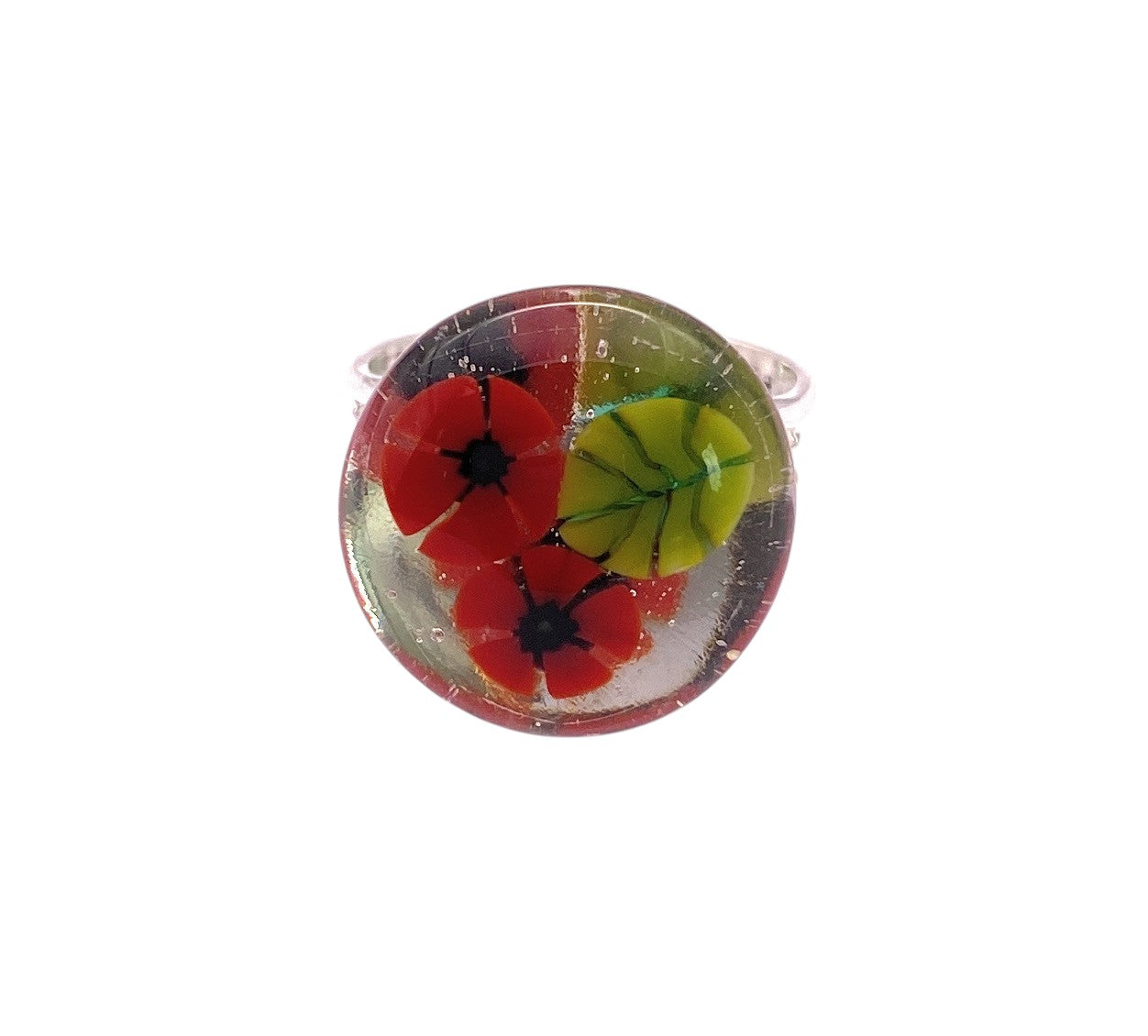 The Calon Glass Poppy Ring (CGR8) is a handmade Millefiori glass flower ring with red petals, black centers, and a green leaf on a silver band, shown against a white background.