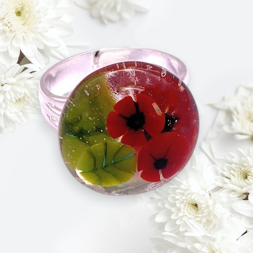 The Calon Glass Poppy Ring (CGR8) is a round handmade glass ring with two red poppy flowers and green leaves inside, in the style of millefiori flower artistry—perfect for nature lovers seeking a unique floral accessory.