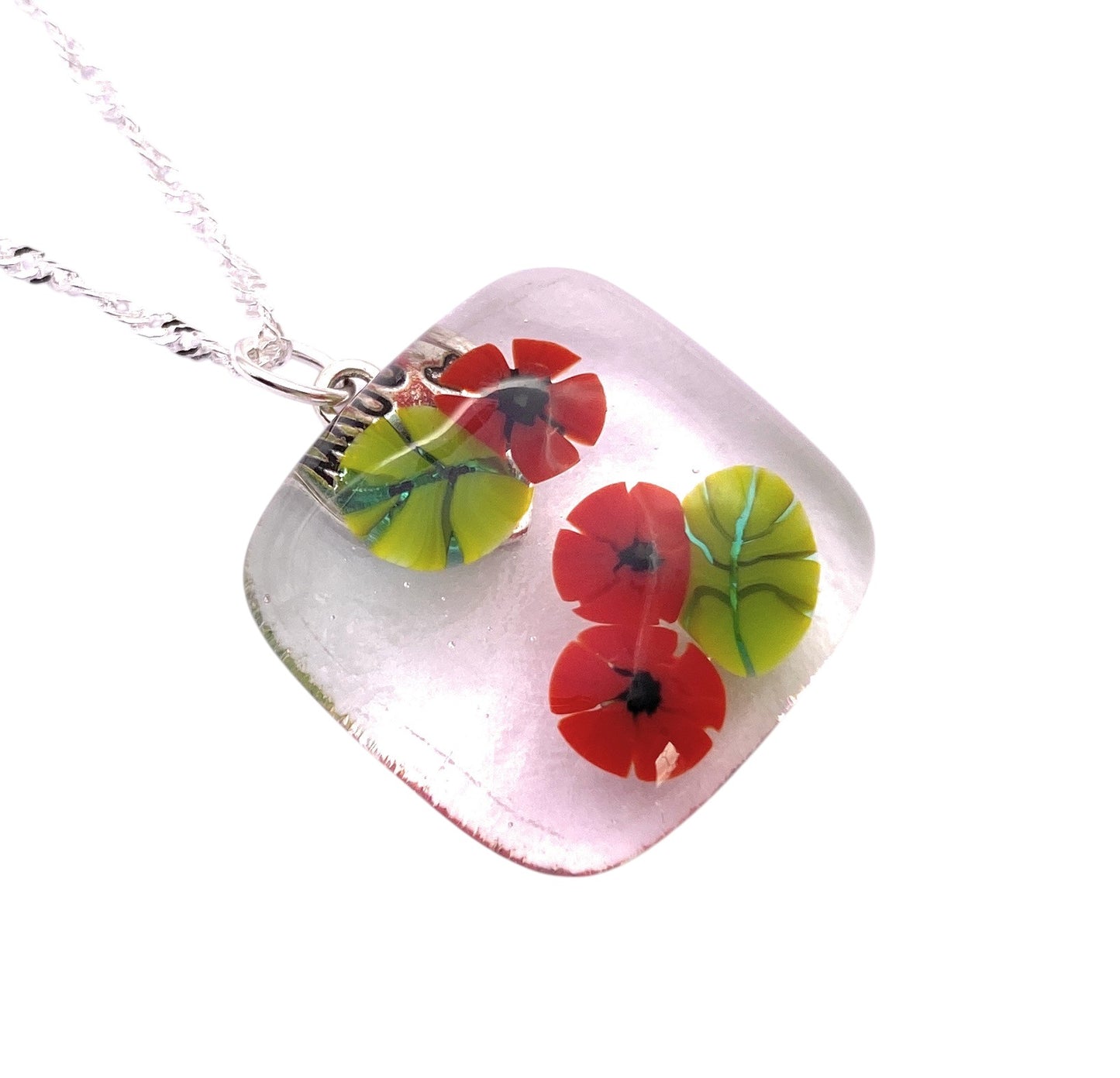 The Poppy Pendant by Calon Glass (CGP29) is a handmade glass pendant with red flower and green leaf designs embedded in clear glass, set on a silver chain.