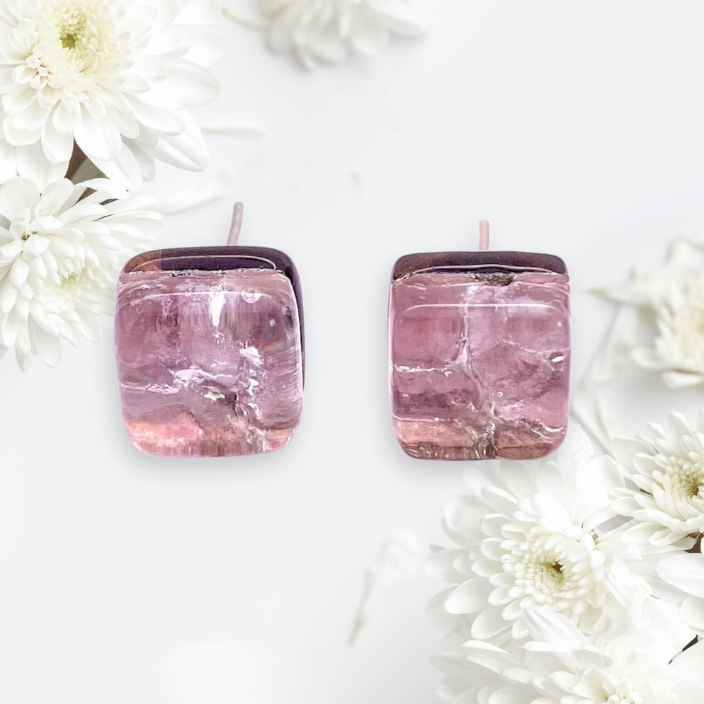 Two square Murano Passion earrings in pale pink/silver, each measuring 8mm in diameter, are elegantly showcased against a light backdrop. White chrysanthemum flowers adorn the corners for added elegance, and their authenticity is guaranteed by a Certificate of Authenticity.