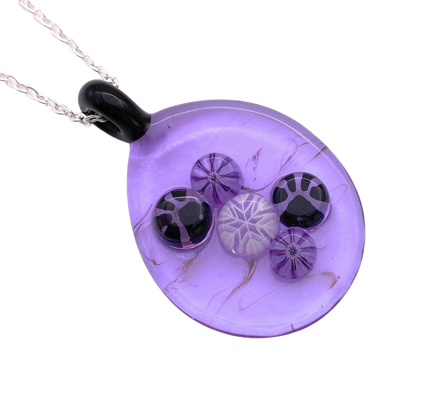 The Calon Glass Handmade Glass Pendant, a teardrop-shaped piece with a deep purple hue, showcases five intricate circular Millefiori glass patterns in black and white. It hangs elegantly on a silver chain with a glossy black top attachment.