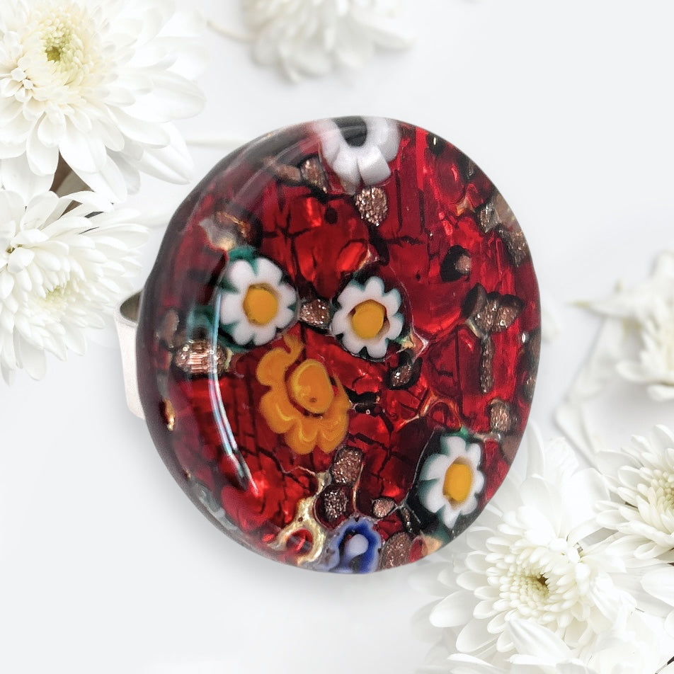 The Murano Passion Millefiori Ring is a 3cm vibrant statement piece featuring a glossy red stone with colorful floral designs among delicate white flowers, highlighting the exquisite craftsmanship of genuine Murano glass.