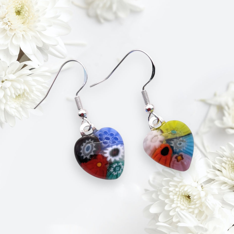 Murano Passion's Murano Glass Earrings feature heart-shaped Millefiori designs with colorful florals. One earring shows blue and black hues, the other red and yellow, both with intricate patterns. Crafted on dainty 1.5cm x 1.3cm frames, they have elegant and durable 925 Sterling Silver hooks.