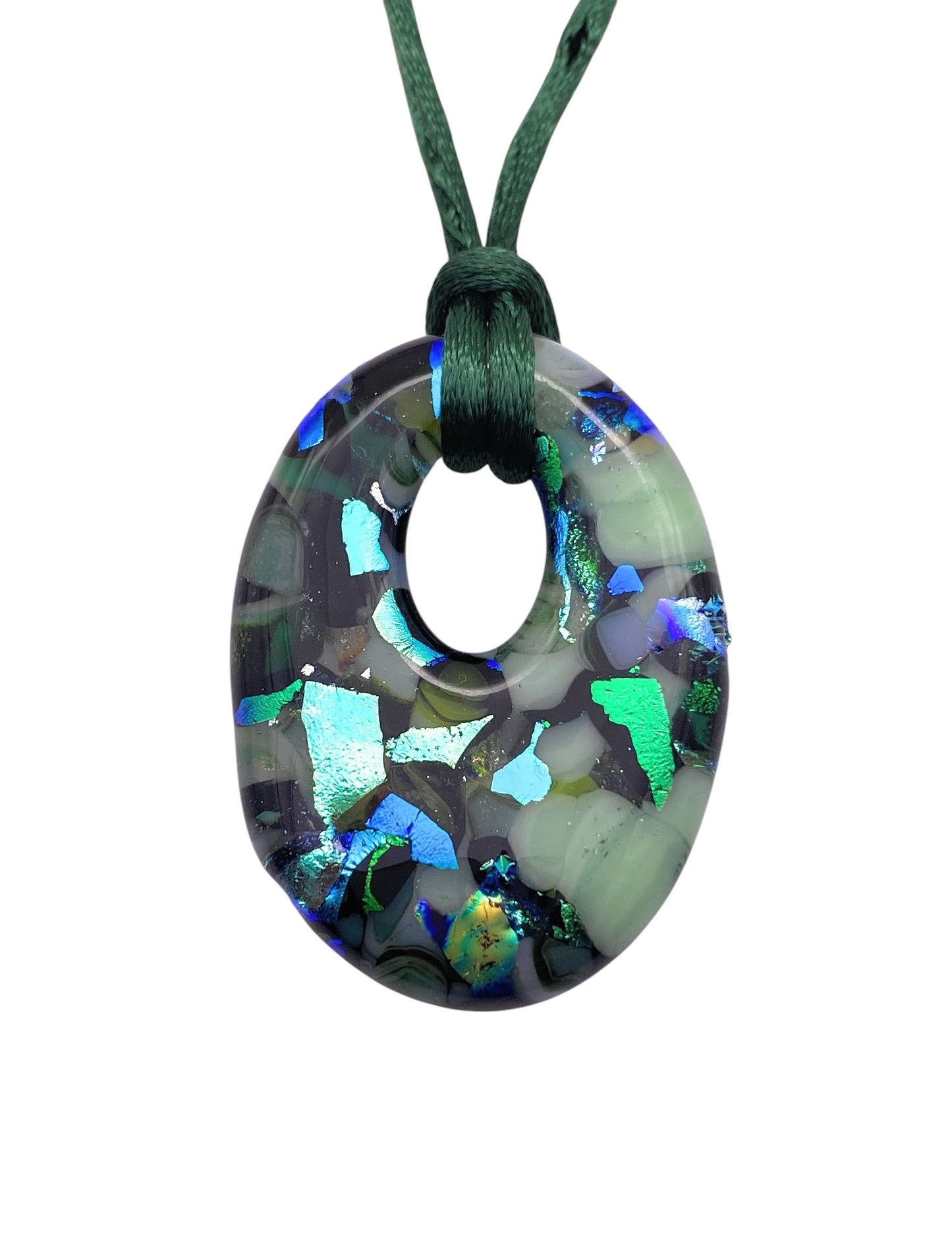 The Handmade Dichroic Glass Pendant by Calon Glass is a round, transparent piece (CGP34) with green and blue iridescent flakes. It elegantly hangs from a dark green cord through its inner circle, contrasting against a white background to enhance its intricate beauty. Size: 4cm x 3cm.