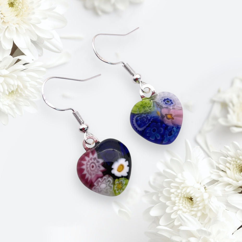 Murano Passion offers Millefiori glass heart earrings with colorful floral designs in blue, pink, green, and white. Accented by 925 sterling silver hooks, these dainty 1.4cm x 1.4cm Murano Glass Earrings are surrounded by white flowers on a light background.