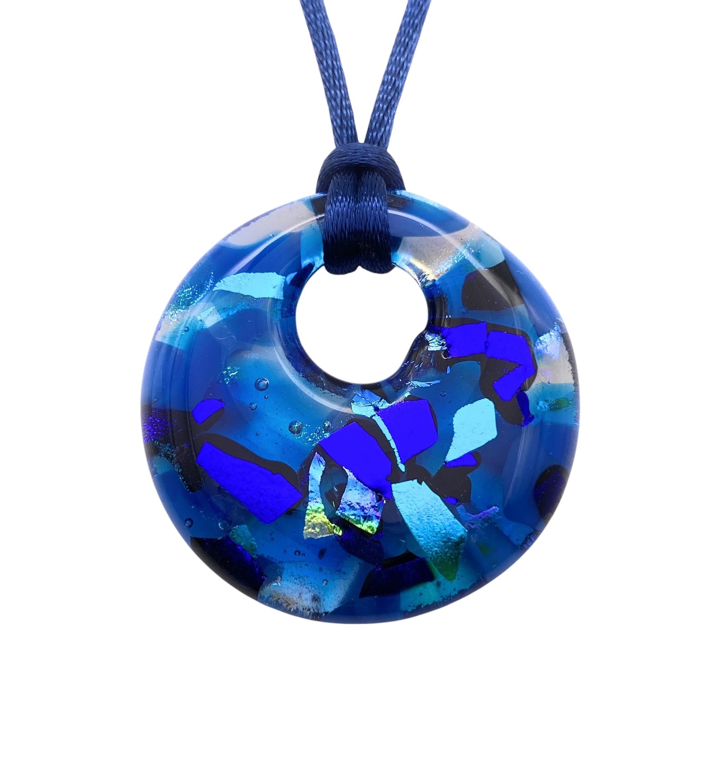 The Calon Glass Handmade Dichroic Glass Pendant (CGP33) is a chunky 4cm piece with ocean-inspired shades of blue, purple, and teal. Strung on a dark blue cord, this kiln-fused, round glass pendant showcases mesmerizing color play.