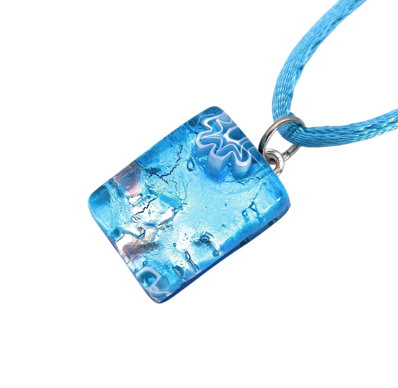 The Murano Passion MGPP18 Pendant features a textured blue glass with abstract patterns, accented by a white swirl and suspended from a silver ring on a blue cord. This unique piece includes a Certificate of Authenticity and measures 2cm x 1.5cm, made using Silver Leaf.