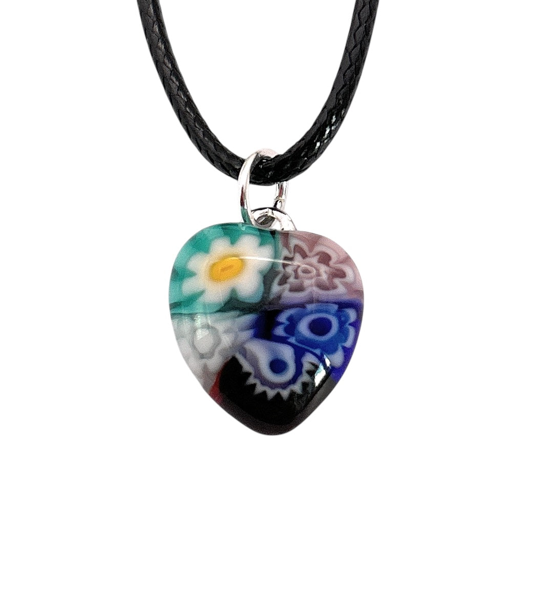 The Murano Passion Murano Heart Pendant (MHT3) features a 1.4cm heart-shaped millefiori design with vibrant green, white, blue, and red flower patterns. It's attached to a black leather cord with a silver loop and includes a Certificate of Authenticity.