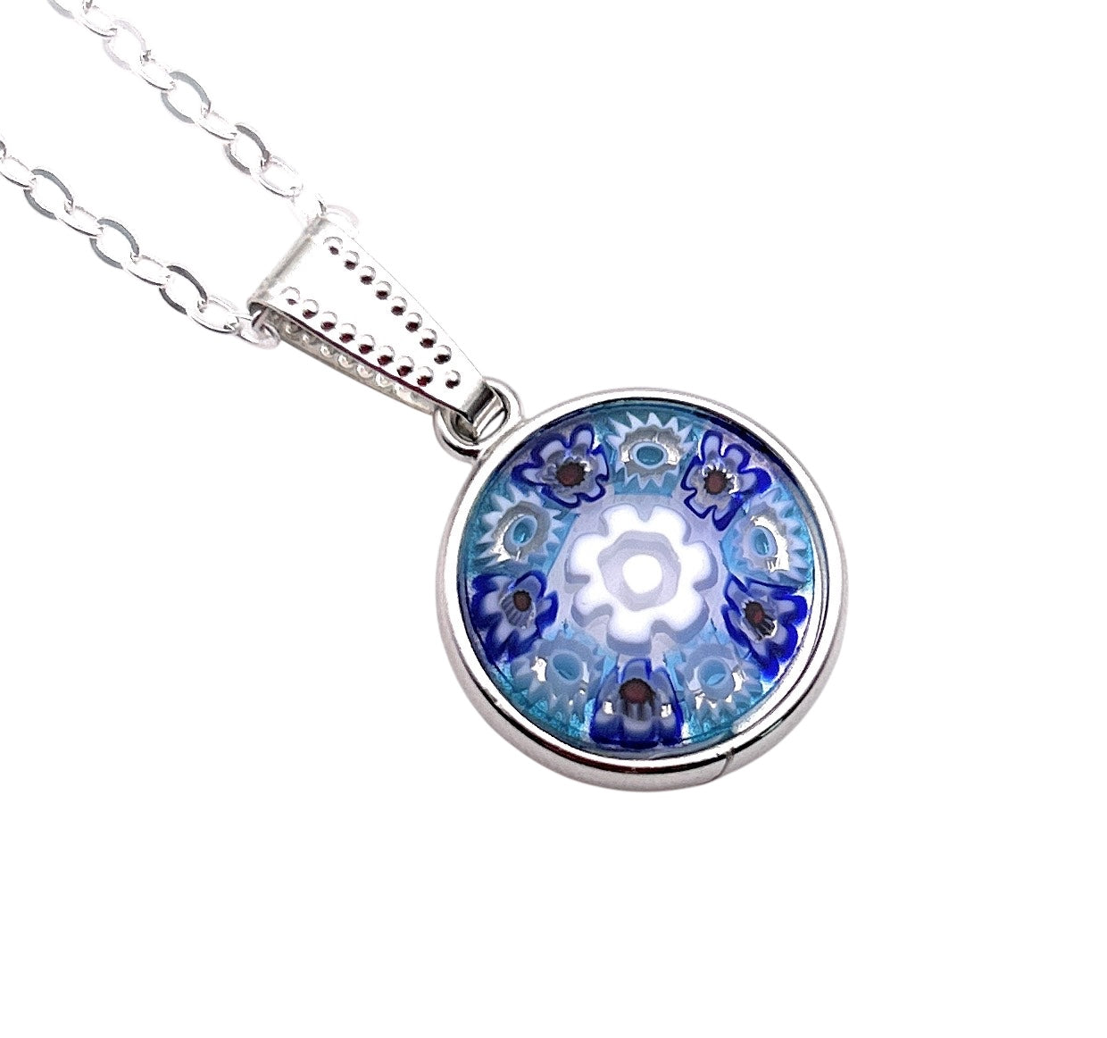 A silver necklace with a round glass charm showcases a blue floral pattern that radiates from the center, resembling the kaleidoscope effect of the Murano Passion Murano Glass Pendant made with Millefiori Flowers - Dainty 1.5cm in shades of blue and white.