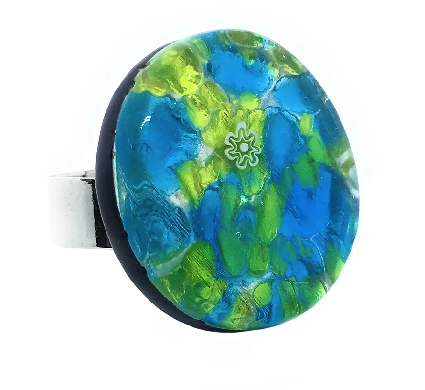A close-up of the Murano Passion's Murano Glass Ring, a chunky 3cm statement piece featuring an oval face adorned with a mosaic of blue and green glass patterns. Handmade in Venice, it highlights a delicate floral motif at the center and is accompanied by a silver-toned band.