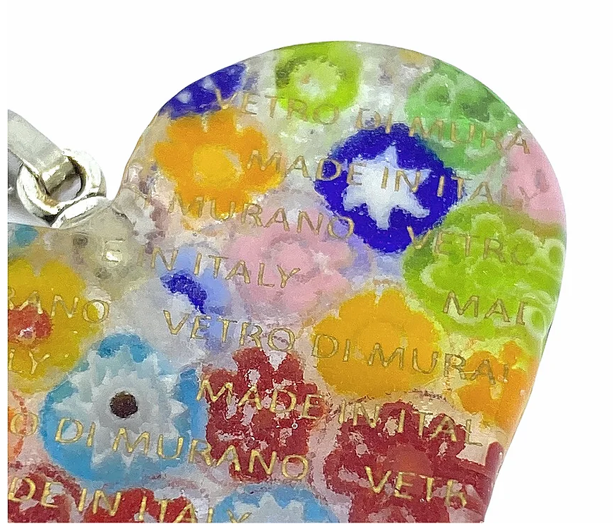 Close-up of a heart-shaped Murano Passion pendant, named the Millefiori Heart Pendant, showcasing vibrant floral designs. Measuring 4cm by 3.5cm, this exquisite piece of Murano Glass Jewelry is inscribed with "Vetro di Murano" and "Made in Italy." It includes a Certificate of Authenticity to ensure its genuine origin.