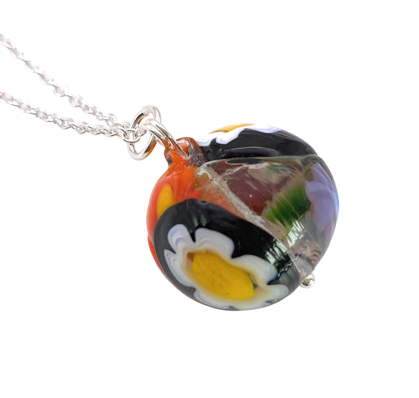 A close-up of the Murano Passion Millefiori pendant from their Multi Coloured collection (MGB1) showcases vibrant floral designs in white, yellow, purple, and red on a clear background. This exquisite piece of Murano Glass Jewellery features intricate patterns reminiscent of Aventurine artistry.