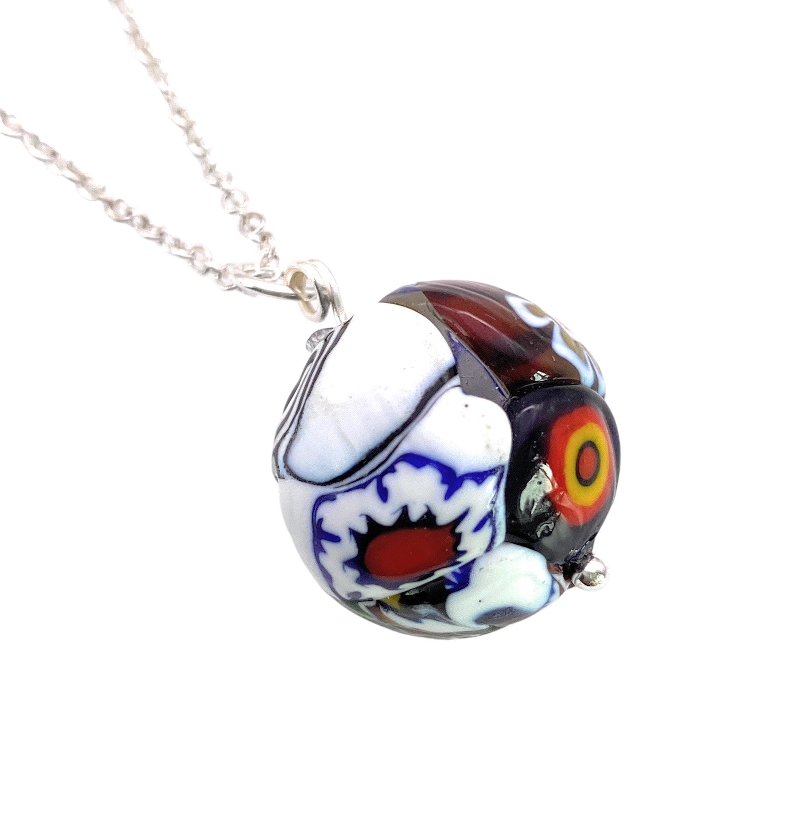 The Murano Passion Murano Glass Multi Coloured Millefiori Ball Pendant (MGB2) is an eye-catching accessory that hangs from a silver chain. It features intricate patterns in blue, red, white, and black on a vibrant glass bead adorned with abstract shapes. This colorful piece includes a certificate of authenticity.