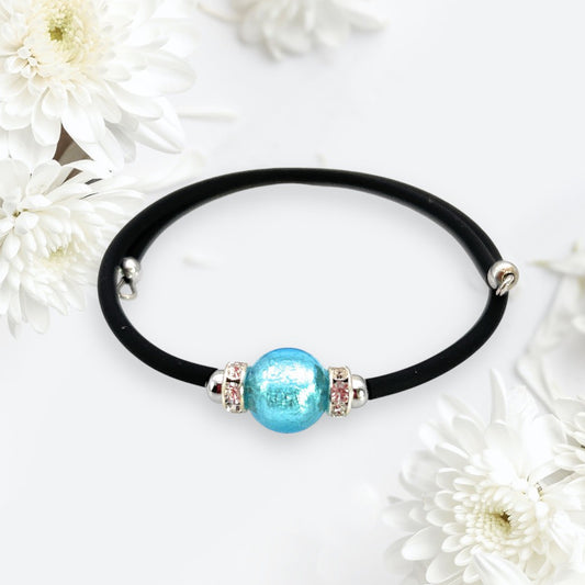 A Murano Passion's handmade Murano Glass Bead Bracelet, showcasing a 1cm blue bead on a memory wire design, is elegantly displayed on a white background surrounded by delicate white flowers.