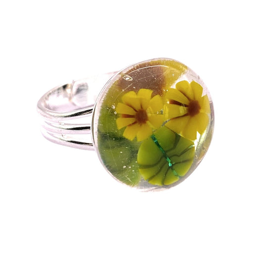 The Sunflower Ring by Calon Glass is a handmade glass Millefiori ring featuring two yellow flowers and a green leaf in clear resin, inspired by sunflowers.