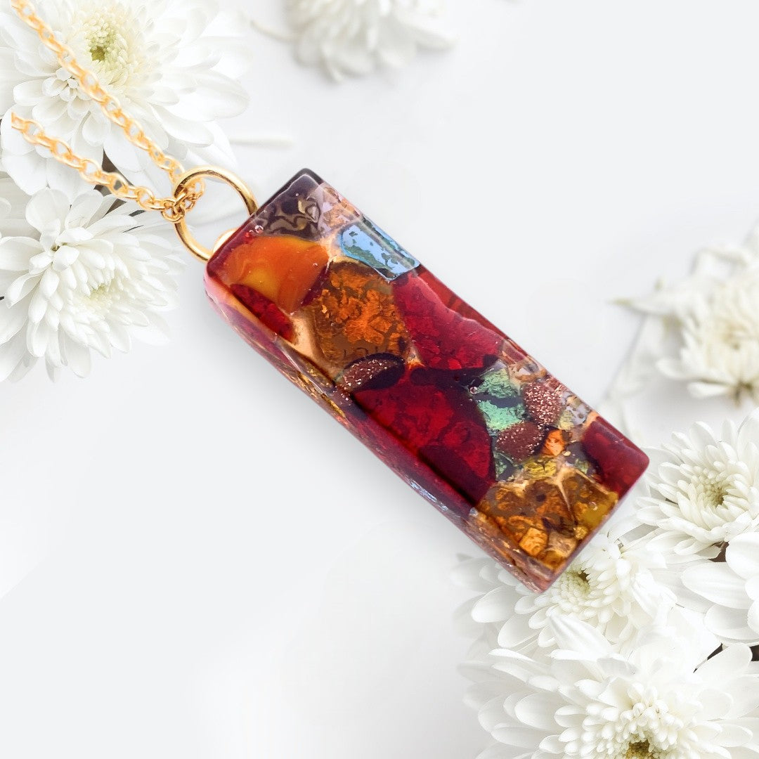 The Murano Passion Murano Glass Pendant (3cm x 1cm, Gold Leaf) hangs on a gold chain, surrounded by white chrysanthemums against a light background.