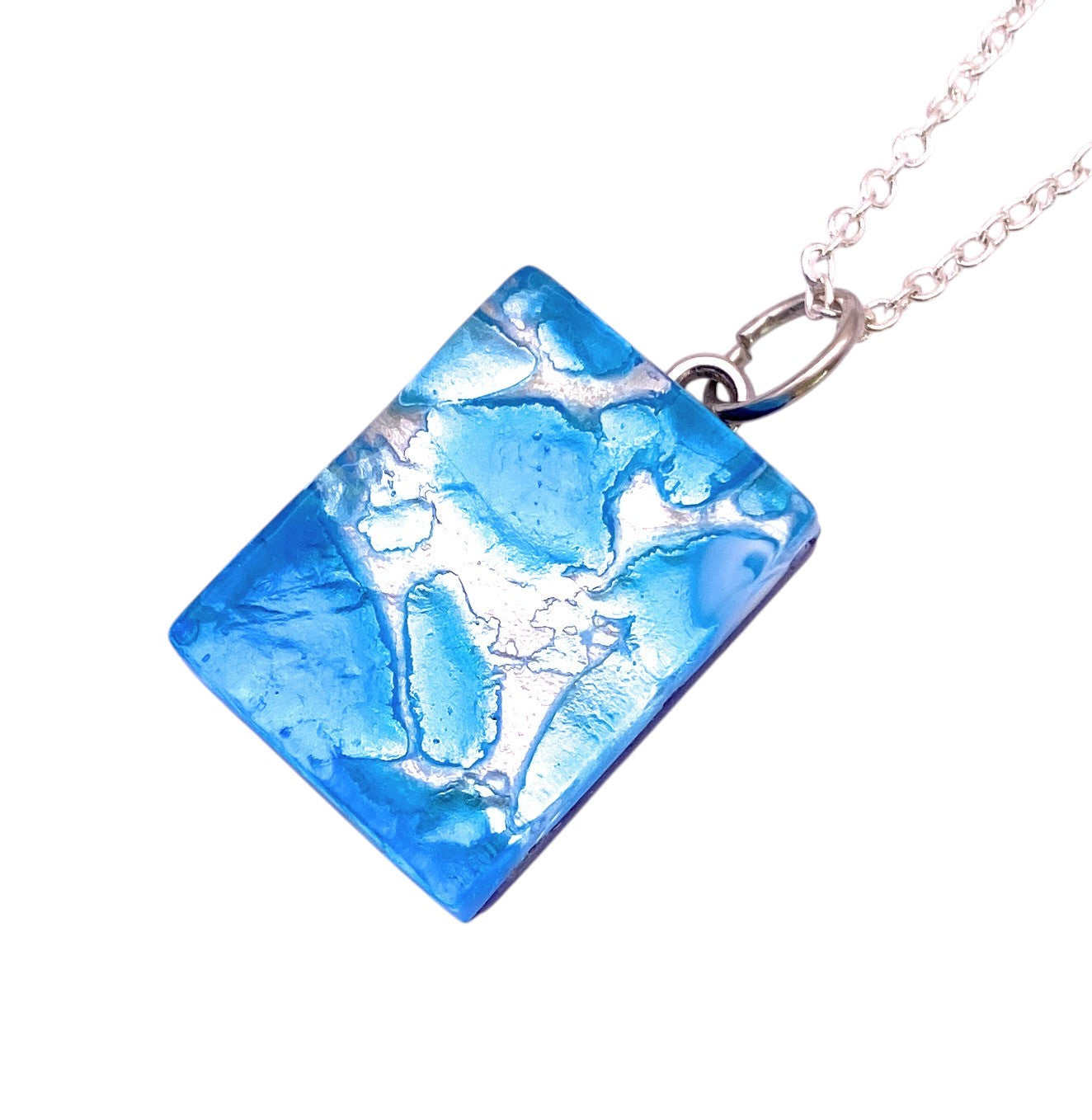 The Murano Passion Murano Glass Pendant, Sky Blue on Silver Leaf (MGPP21), is a dainty 2cm x 1.5cm rectangular pendant featuring abstract white patterns on striking sky blue glass, suspended from a silver chain—perfect for admirers of unique Murano Glass jewellery.