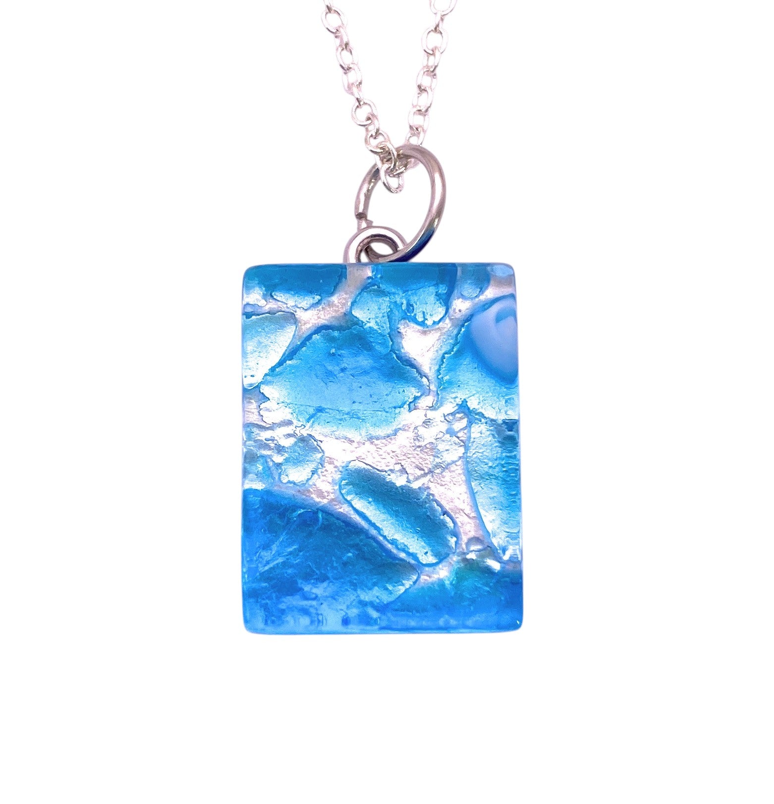 Discover the Murano Passion “Murano Glass Pendant, Sky Blue on Silver Leaf”—a dainty 2cm x 1.5cm rectangular pendant adorned with enchanting sky blue hues over shimmering silver leaf, gracefully suspended from a silver chain—an exquisite piece of Murano Glass Jewellery.