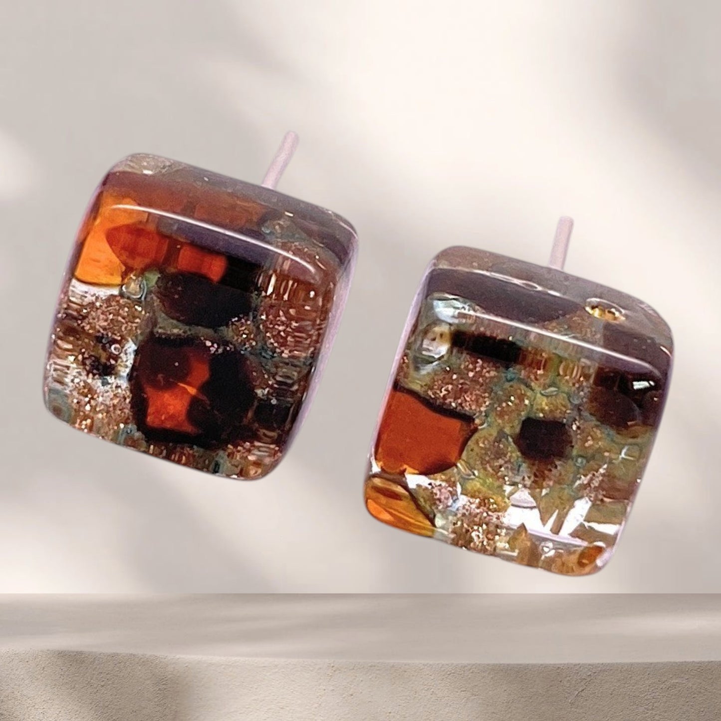 The Murano Passion Murano Glass Earrings - Multi on Gold (MGE1) feature dainty 8mm squares with amber, gold, and dark accents in a glossy finish, shown against a neutral, softly lit background.