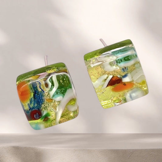 Murano Passion’s dainty 8mm Murano Glass Earrings – Multi on Gold (MGE9) showcase abstract green, yellow, orange, and blue patterns against a neutral backdrop—a stunning example of authentic Murano artistry.