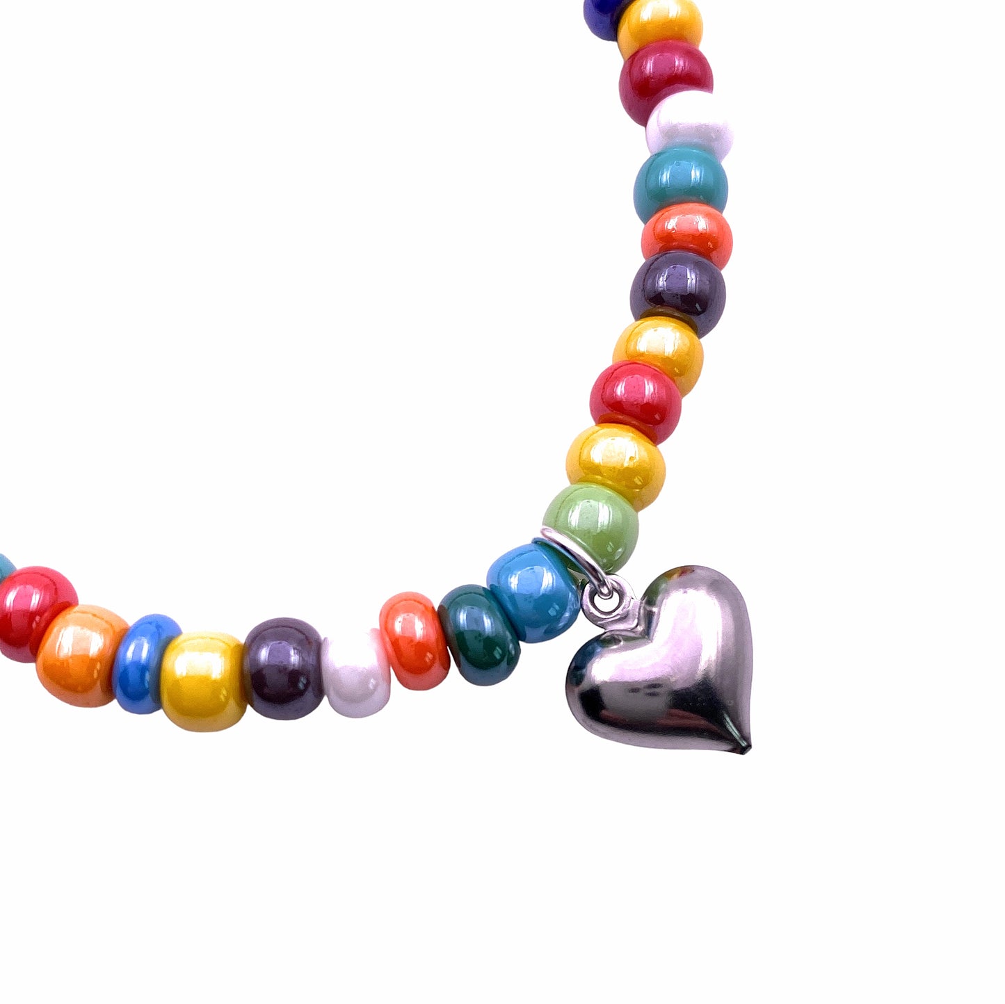 The Murano Passion Murano Glass Beaded Bracelet with Heart Charm (MGBR7) showcases an array of vibrant 5mm multi-coloured beads in shades such as red, yellow, blue, green, and orange. An elegant silver heart charm delicately hangs from the elasticated bracelet against a plain white backdrop.