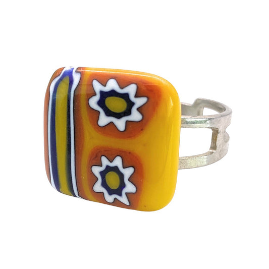 This silver adjustable Murano Glass Ring from Murano Passion, measuring 1.5 cm, draws inspiration from Venetian artistic heritage. It showcases a vibrant square face with striking orange and yellow stripes on one side and two white and blue millefiori glass flowers set against a yellow background on the other side.