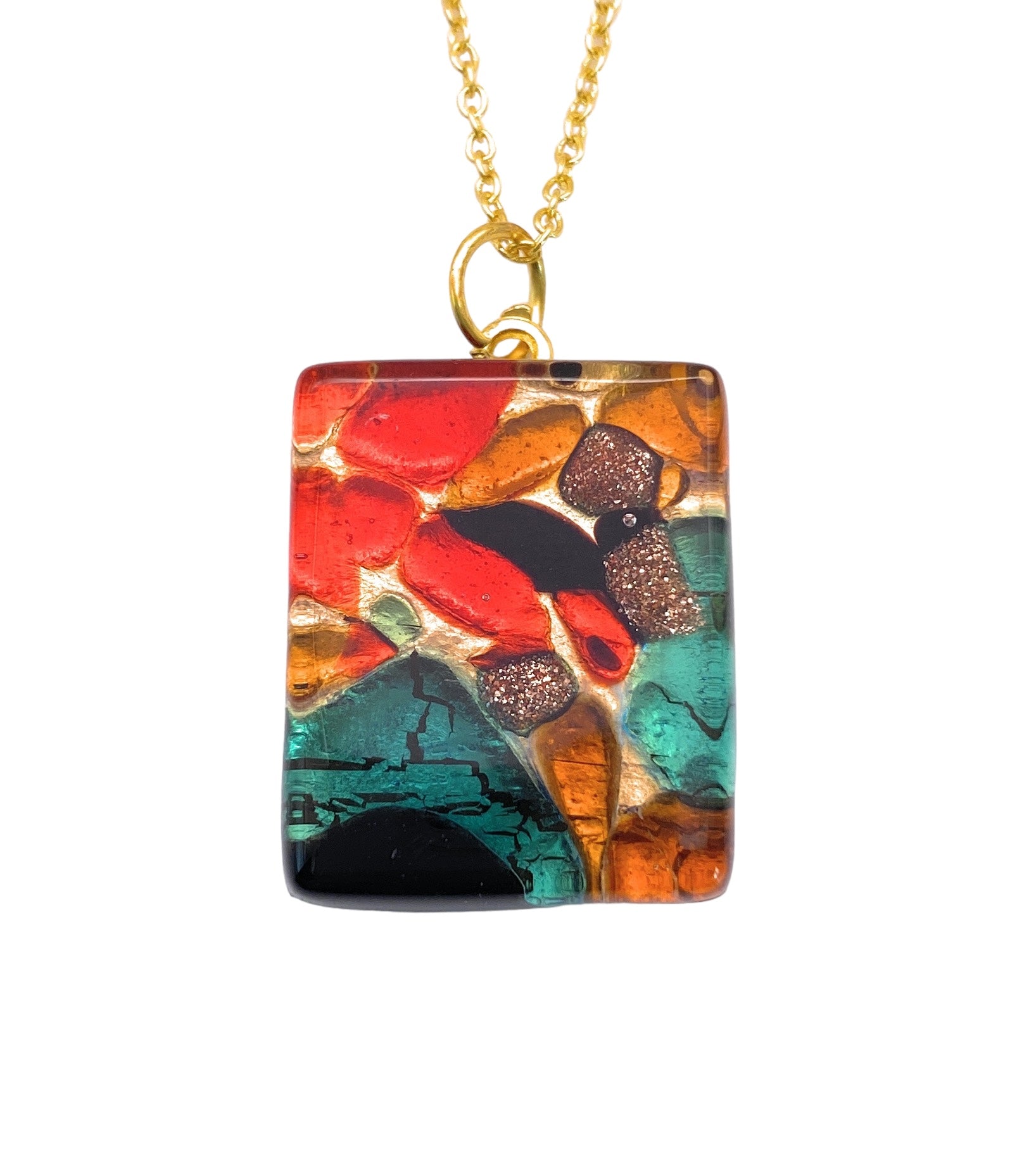 Introducing the Murano Passion's Murano Glass Pendant on Gold Leaf, measuring 2.5cm x 2cm, this exquisite piece features a rectangular pendant with a gold chain and showcases an abstract design in vibrant red, orange, teal, and black tones. Handmade in Italy, its colorful patterns deliver an artistic and lively aesthetic.