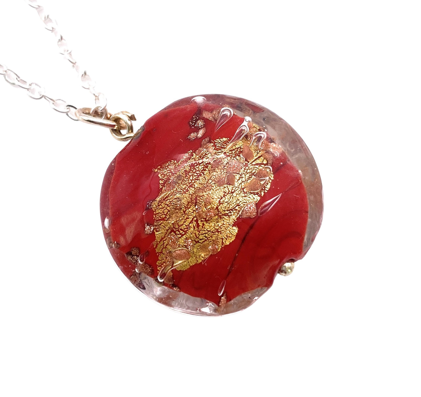 The Murano Passion circular pendant features a gold leaf pattern set against a rich red background and hangs from a silver chain. Evocative of traditional Murano Glass Jewellery, the design showcases swirling gold details. This 2.5cm handmade glass bead pendant has a glossy finish and includes a Certificate of Authenticity.