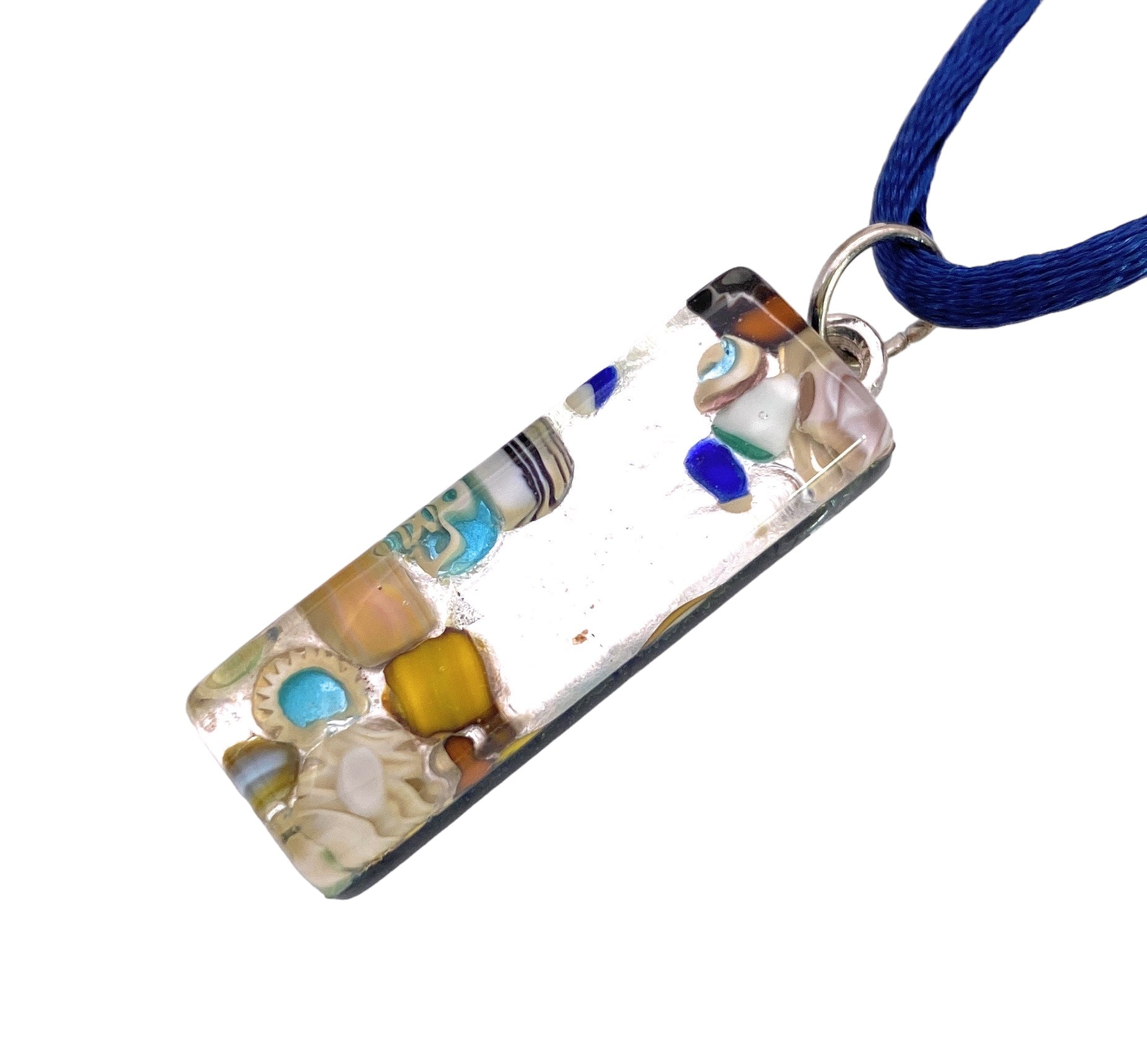 The Murano Passion pendant, featuring a vibrant mosaic pattern of yellow, blue, and white hues that exemplifies Millefiori design, is crafted from clear resin embedded with colorful beads and small objects. Hanging from a blue cord, this rectangular piece measures 3cm x 1cm and includes a Certificate of Authenticity.