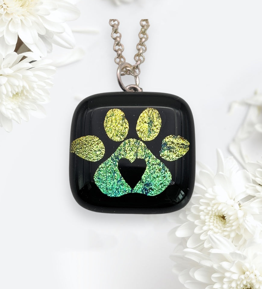 A pendant necklace features a green paw print design with a heart shape on black glass, surrounded by white flowers