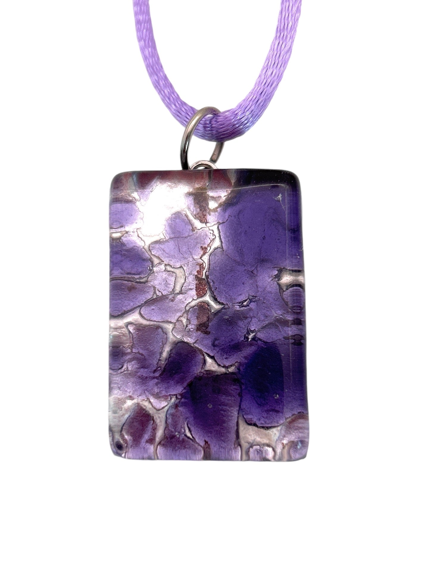 The Murano Passion Murano Glass Pendant, Millefiori Flower Pendant on Silver Leaf (3cm x 2cm) (MGPC2), includes a Certificate of Authenticity and features a rectangular design adorned with a violet floral pattern. It is suspended from a purple cord, displaying intricate shades of purple and silver for an elegant and textured artistic appearance.