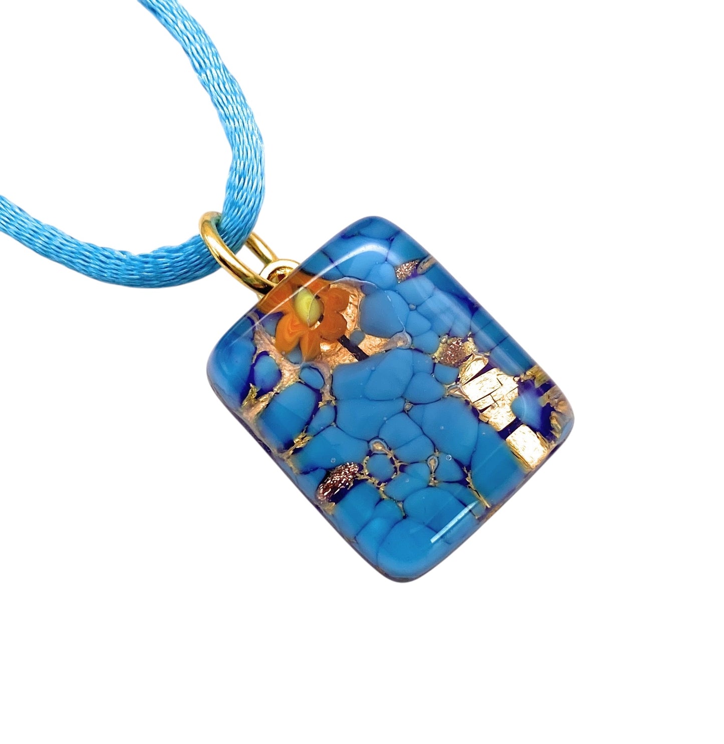 This exquisite Murano Passion pendant, featuring a dainty 2cm x 1.5cm rectangular design, showcases blue on gold leaf adorned with orange floral accents. It hangs elegantly on a light blue cord necklace, adding a touch of Venetian charm. A Certificate of Authenticity ensures the genuine artistry of this Murano Glass creation (MGPP28).