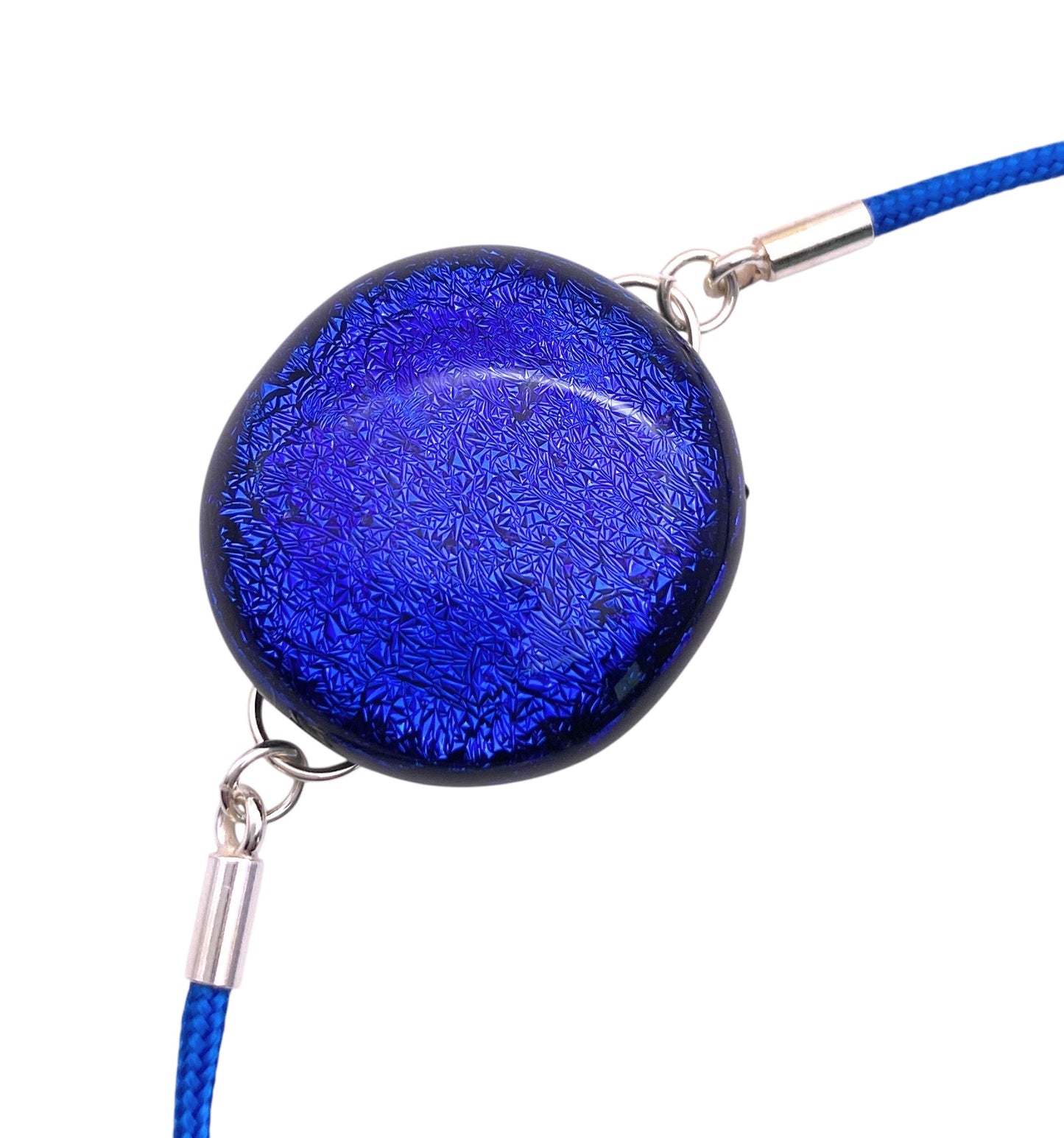 A 2cm handmade dichroic glass pendant by Calon Glass is attached to a braided blue cord, featuring a leaf-like pattern and metallic clasps, creating an artisanal feel.