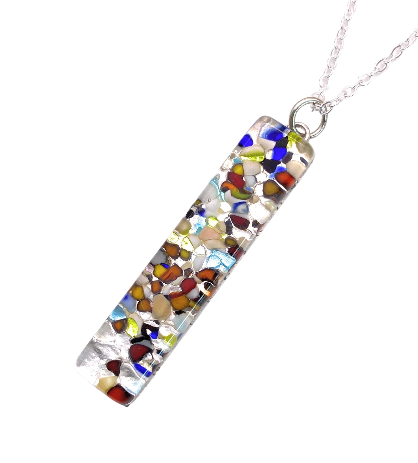 The "Murano Glass Pendant on Silver Leaf" by Murano Passion features a 4cm x 1cm rectangular design with vibrant, abstract mosaic patterns in blue, red, yellow, and white. It is embellished with Millefiori elements and hangs gracefully from a silver chain.