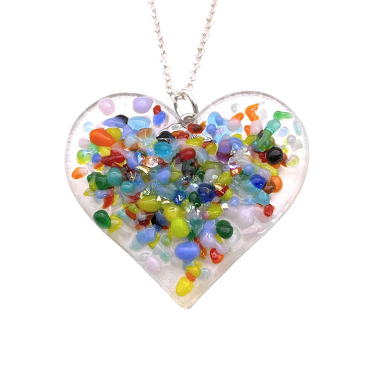 A charming heart-shaped pendant crafted by Calon Glass features a delightful arrangement of handmade dichroic glass beads in joyful shades of blue, green, red, and yellow. These beads are beautifully scattered to form a mosaic-like pattern on the 3.5cm x 3.5cm pendant that elegantly hangs from a silver chain.