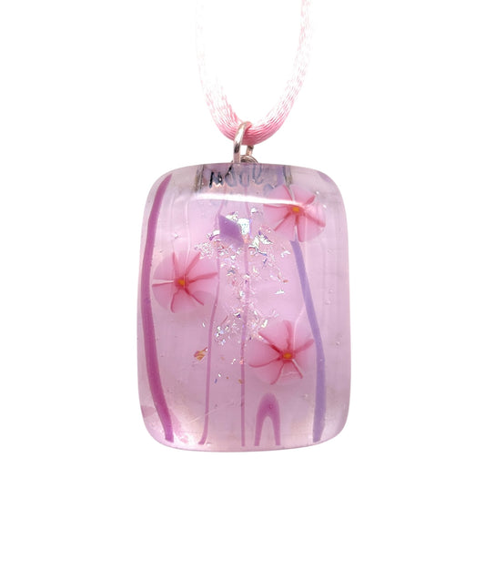 The Handmade Dichroic Glass Pendant by Calon Glass, featuring pink Millefiori flowers with silver specks and purple swirls, elegantly hangs from a light pink cord. The pendant measures 3cm x 2cm (CGP3).