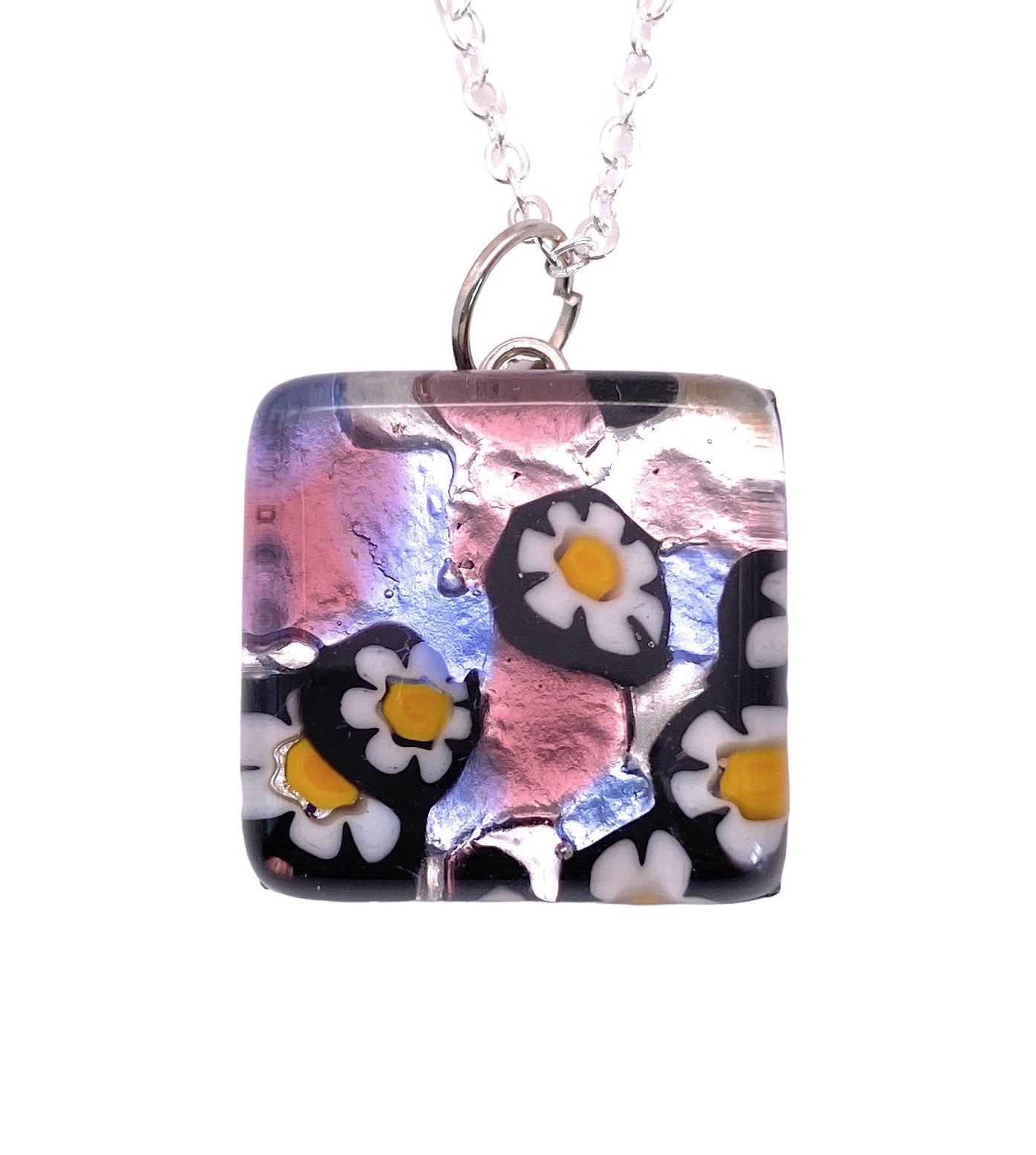 Murano Passion's Millefiori Flower Pendant on Silver Leaf is a stunning square glass piece, measuring 2cm x 2cm, designed with a captivating blend of white and yellow flowers set against swirling pink, blue, and silver hues. This genuine Murano glass pendant comes with a certificate of authenticity and hangs elegantly from a silver chain.