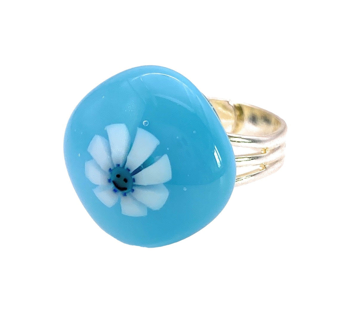 The Calon Glass Handmade Glass Ring features a smiley face Millefiori flower design, beautifully showcased in the center of its silver band.