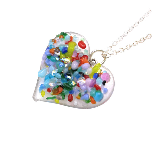 The Handmade Heart Pendant by Calon Glass is a beautifully crafted dichroic glass piece, measuring 2.5cm x 2.5cm, featuring an array of colorful, irregularly shaped beads and crystals, all elegantly suspended from a silver chain against a white background.