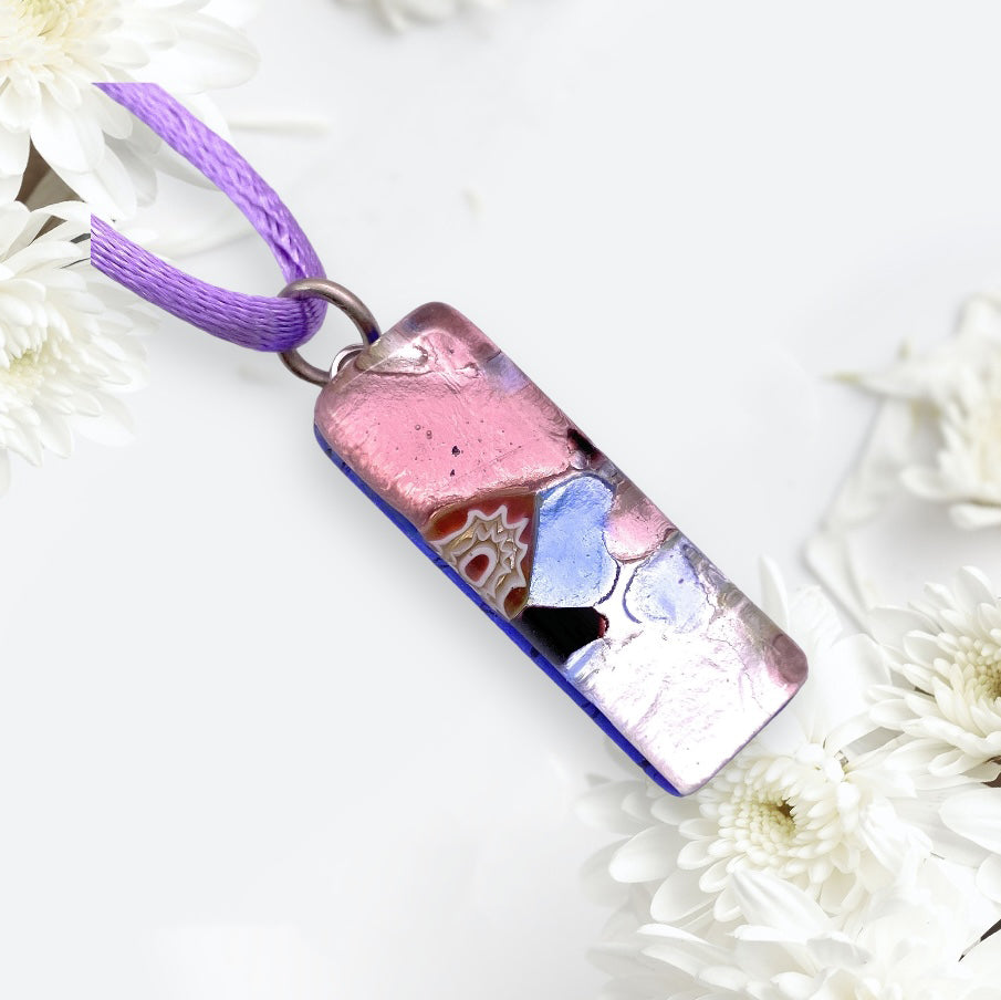 The Murano Passion Murano Glass Pendant on Silver Leaf (3cm x 1cm, MGPL15) showcases an elegant and unique design with a pink, blue, and silver abstract pattern hanging from a purple cord. This exquisite piece of jewellery is beautifully enhanced by white daisies on a light background.