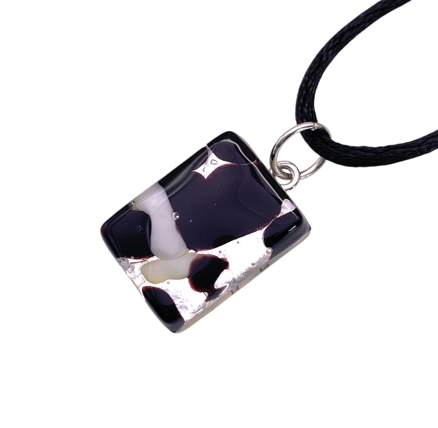 Introducing the Murano Glass Pendant by Murano Passion, a dainty 2cm x 1.5cm piece graced with an abstract black, white, and red pattern. This pendant hangs elegantly from a black cord necklace, crafted in the iconic style of Murano Glass Jewellery. It features a glossy finish and is accented with a silver attachment loop.