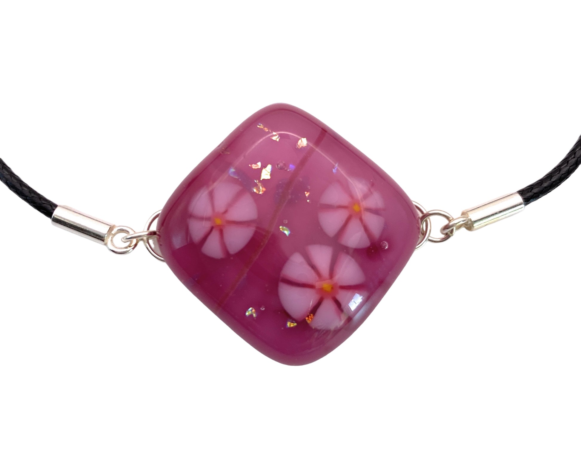 The Calon Glass CGBR1 bracelet showcases a handmade dichroic glass pendant with pink and white Millefiori flowers accentuated by gold flakes, secured to a black cord with silver clasps.