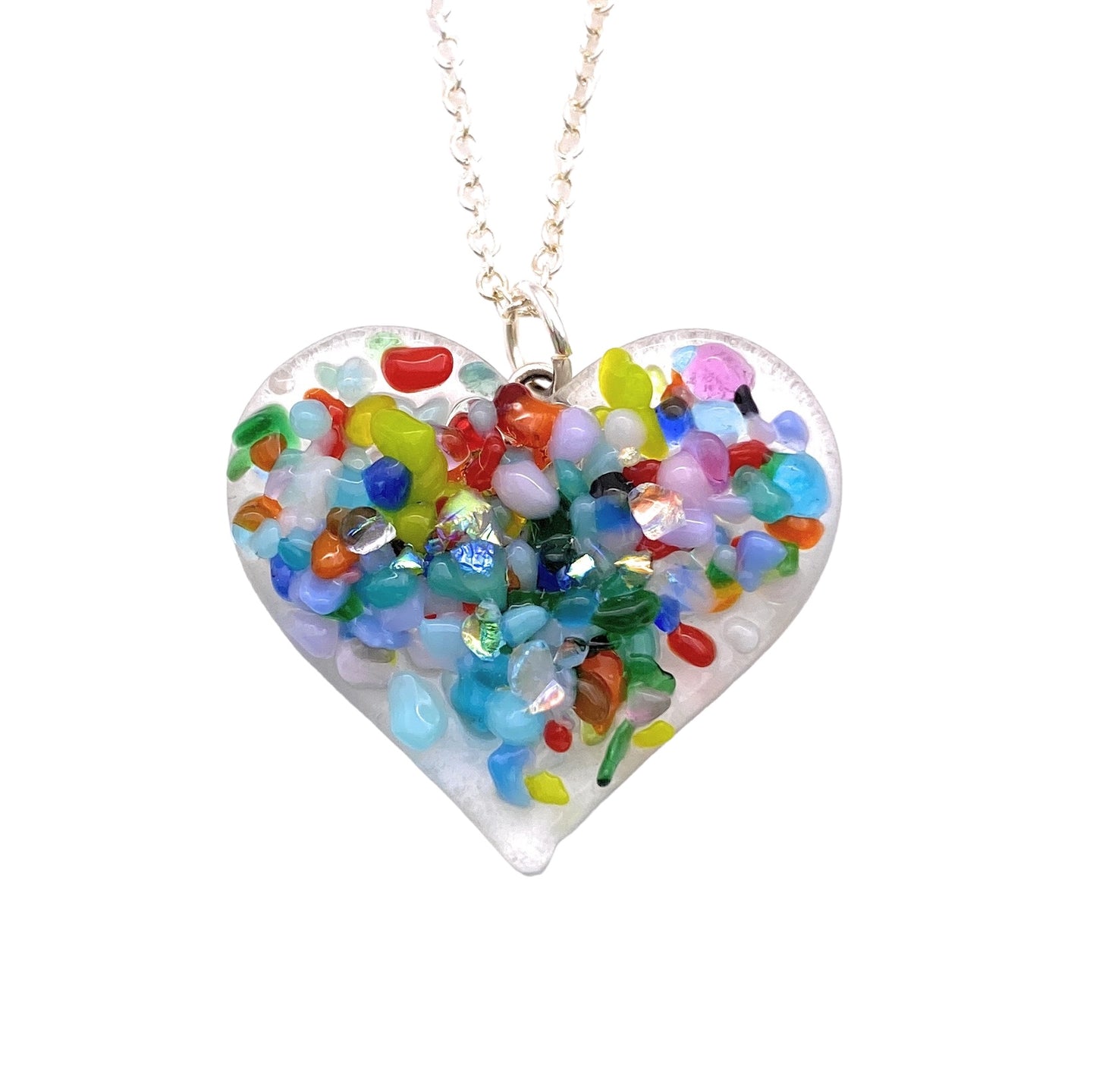 The Handmade Heart Pendant by Calon Glass features a dainty 2.5cm x 2.5cm design crafted from handmade dichroic glass, beautifully adorned with an array of colorful stones. Hanging elegantly on a delicate silver chain, the stones inside glisten in vibrant shades of red, blue, green, orange, and purple.