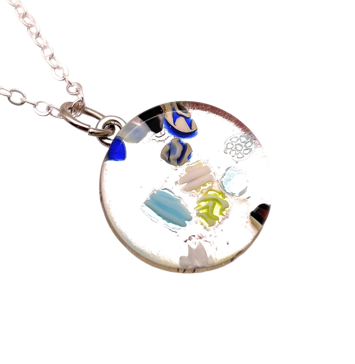 A Murano Glass Round Pendant by Murano Passion, featuring Millefiori with colorful abstract patterns in blue, yellow, green, and beige details hangs from a silver chain against a white background.