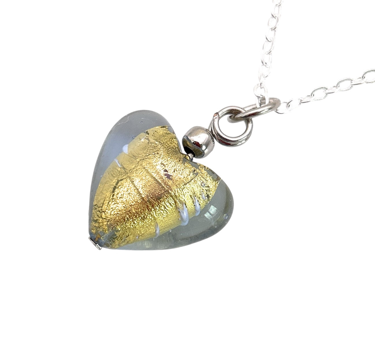 This Murano Passion Murano Heart Pendant (MHT13) showcases a delicate gold leaf design within, gracefully hanging on a silver chain. Each pendant is accompanied by a Certificate of Authenticity, guaranteeing its distinctive craftsmanship and true elegance.