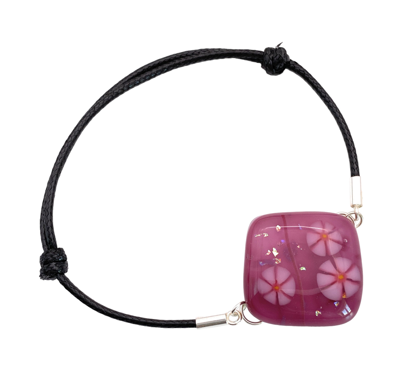 The Calon Glass Handmade Dichroic Glass Bracelet (CGBR1) features a square black cord with a pink Millefiori floral glass bead and gold flakes, set on an adjustable silver-clasped cord. Ideal for both casual or chic outfits.