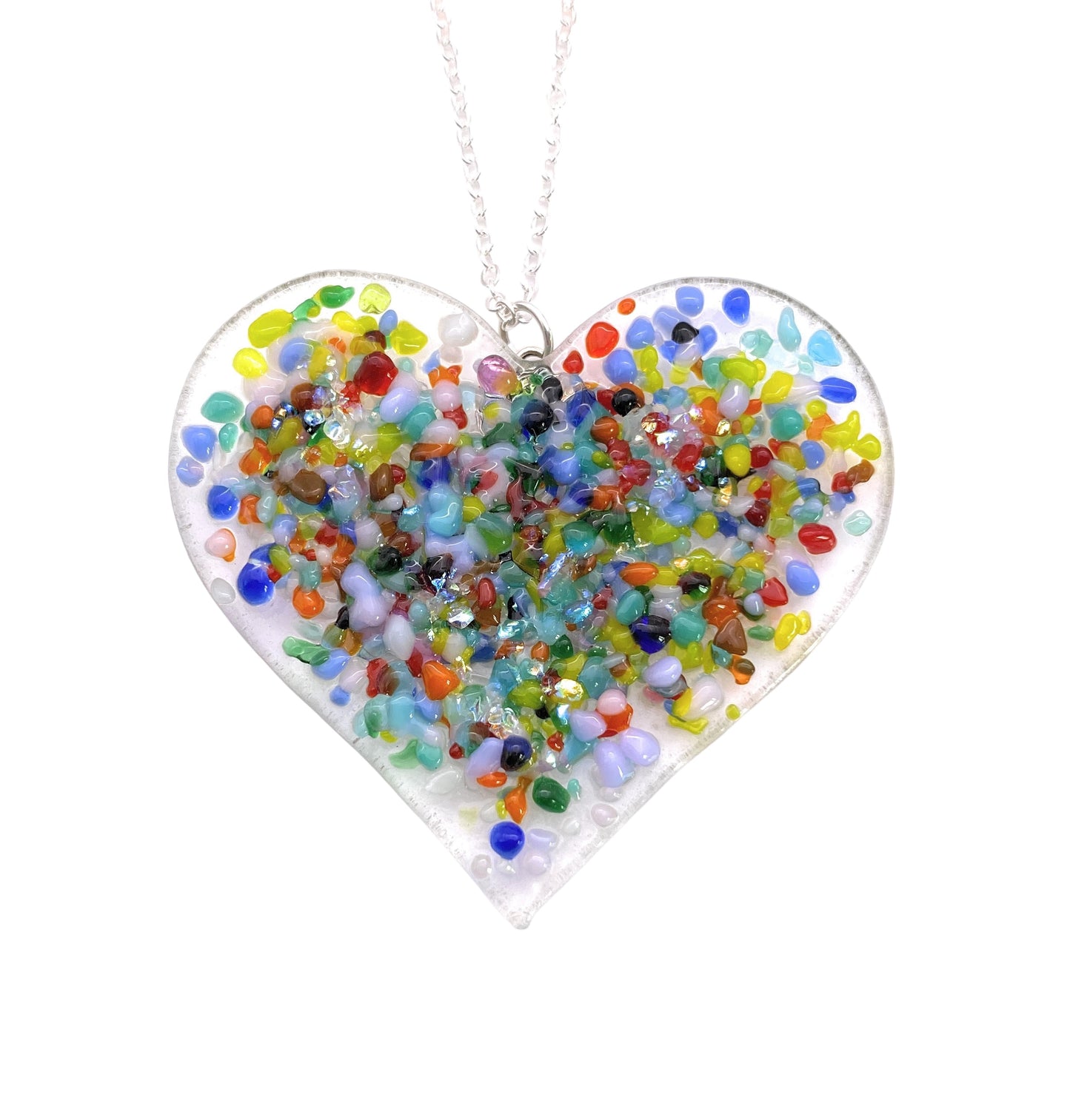 The "Chunky Handmade Heart Pendant" by Calon Glass features a heart-shaped design with a clear base, filled with small, colorful beads made of dichroic glass. These vibrant beads showcase hues of red, blue, green, and yellow. The exquisite handmade pendant measures 6cm x 4cm and elegantly hangs from a silver chain.