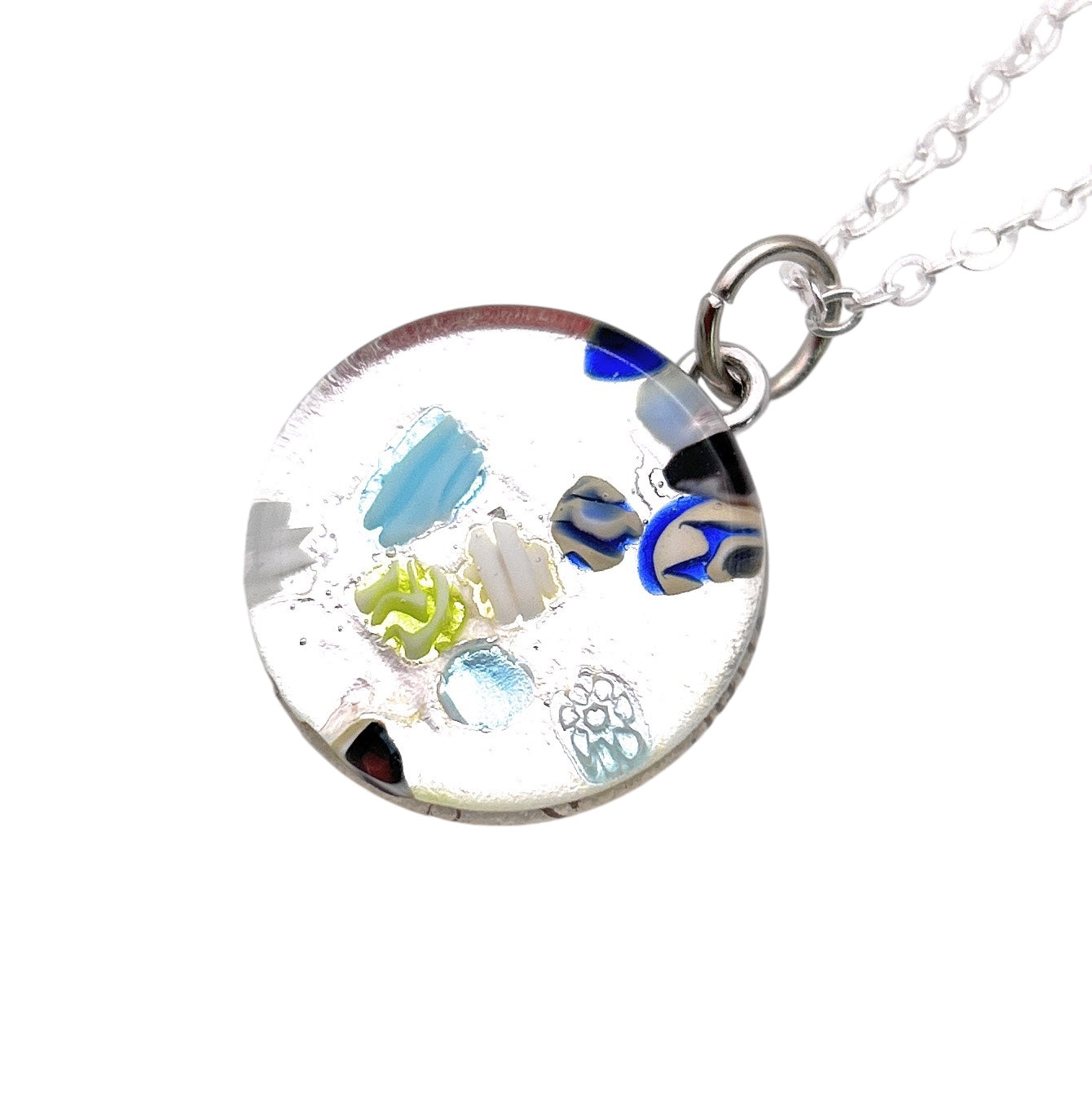 The Murano Passion Murano Glass Round Pendant, made with Millefiori and measuring 2cm (MGPV21), features a stunning mosaic of colorful patterns in blue, green, and black designs. It hangs from a delicate silver chain and comes with a Certificate of Authenticity.